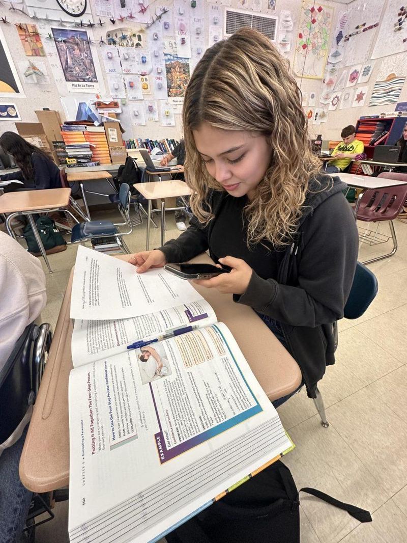 A student with a textbook open and a phone in hand